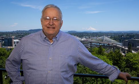 Les AuCoin stands in front of the Portland skyline with Mt Hood in the background