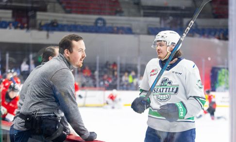 Tom Orr stands on the Seattle Thunderbirds bench and talks with hockey player Ashton Cumby.