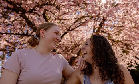 Two students sit in front of a flowering cherry blossom tree on Pacific's Forest Grove Campus.