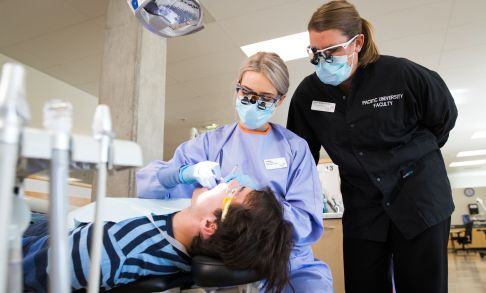 A dental hygiene students cleans a patient's teeth under the supervision of a faculty member.