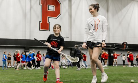 A woman teaches a young girl how to use a Lacrosse stick during the women and girls in sports event at Pacific's Stoller Center.