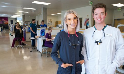 Two dental hygiene students, one male and one female, pose in the dental hygiene teaching space.