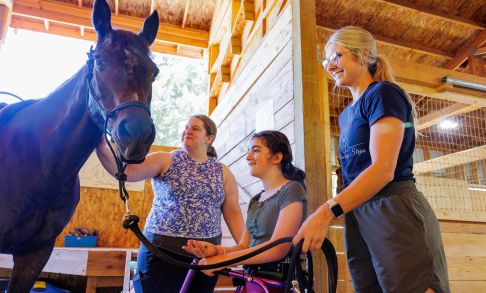 Pacific occupational therapy alumni students lead a disabled child toward a horse during an equine therapy session.