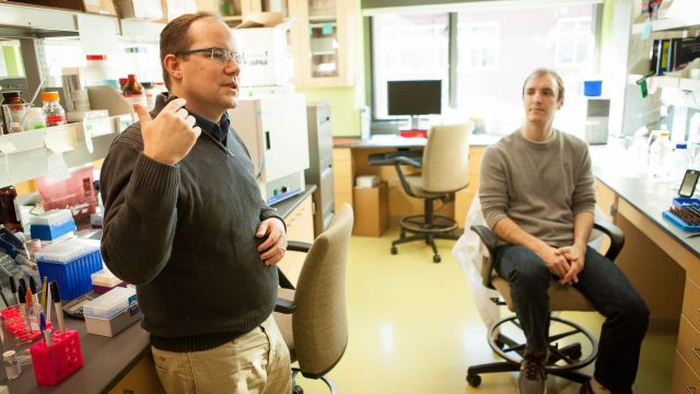 A pharmacy professor speakers to students in a pharmacy lab setting.