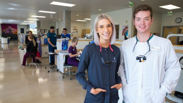 Two dental hygiene students, one male and one female, pose in the dental hygiene teaching space.