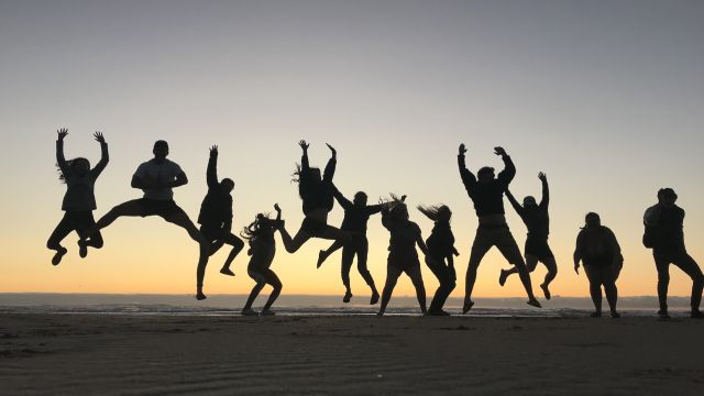 Pacific students jumping up in the air in silhouette against a sunset