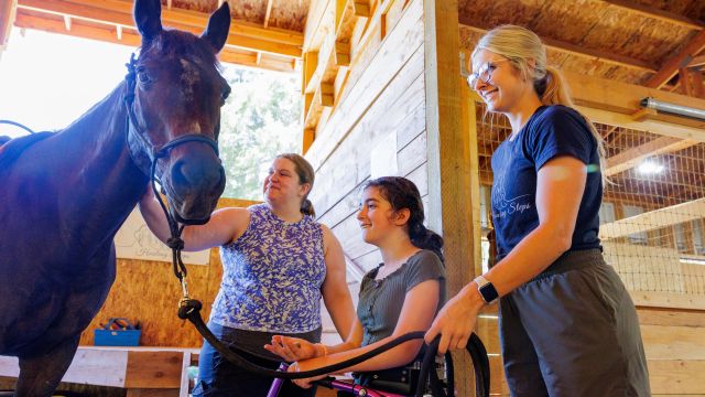 Pacific occupational therapy alumni students lead a disabled child toward a horse during an equine therapy session.