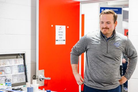 Tom Orr stands next to a sign on the medical room door that reads "Visitors Medical Room".