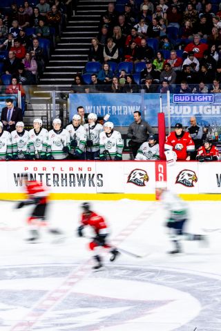 Photo of the Seattle Thunderbirds bench and Tom Orr watching the game as hockey players skate by in a blur.