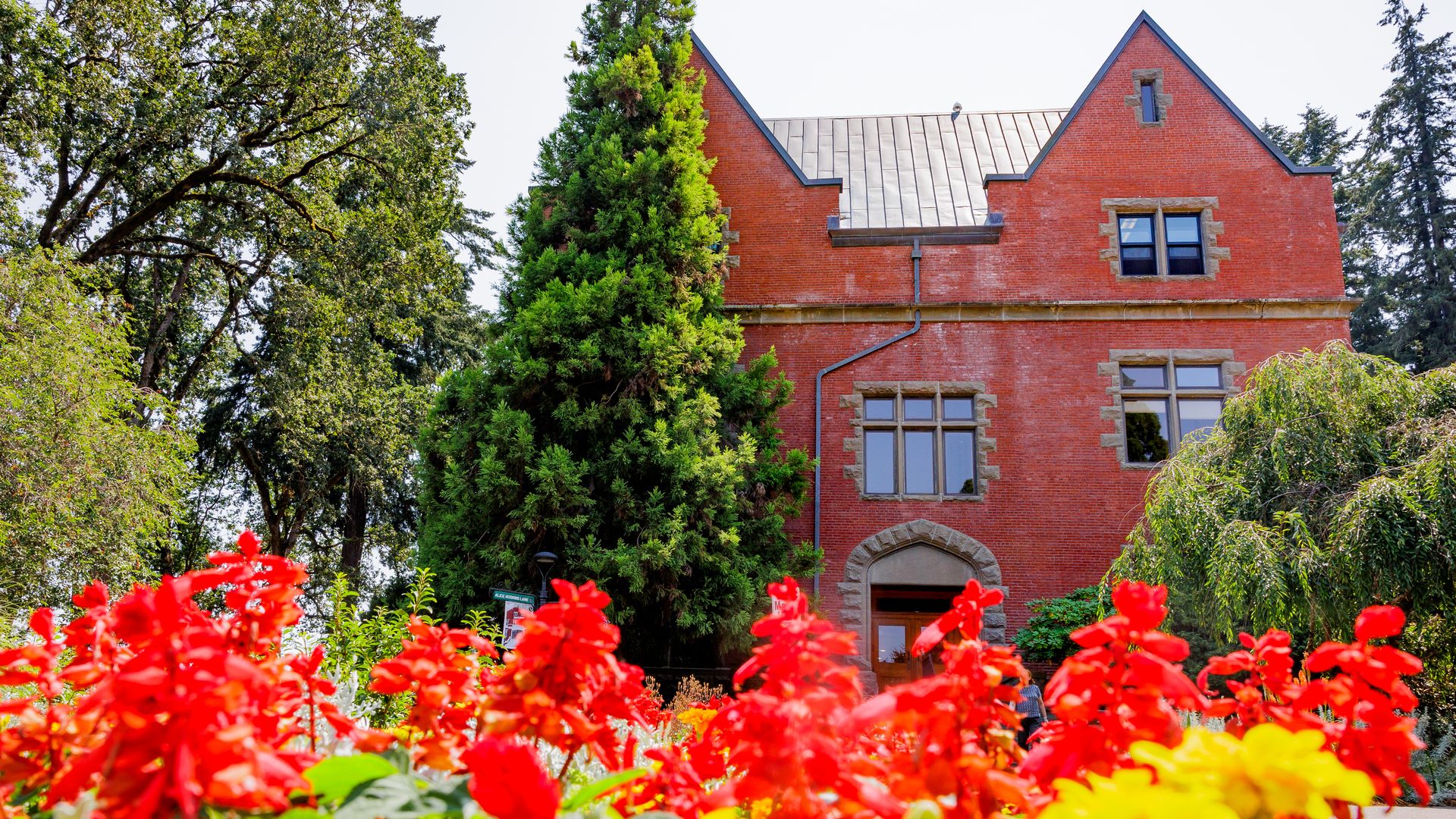 Red and yellow flowers bloom in front of Pacific University's Marsh Hall